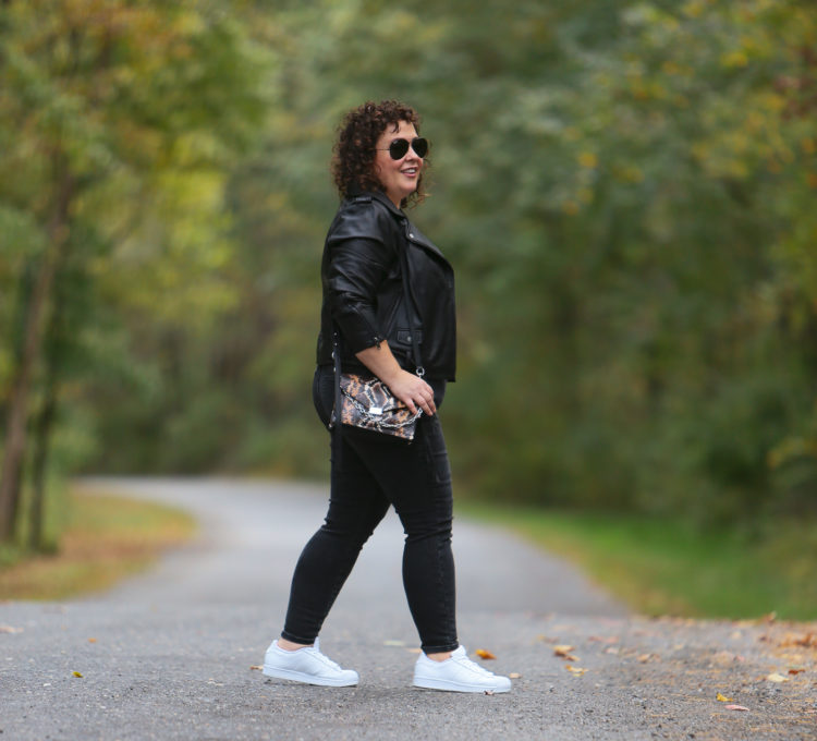 Alison in a black leather moto jacket, black and cream striped tee, gray jeans and white sneakers walking a small brown and white dog