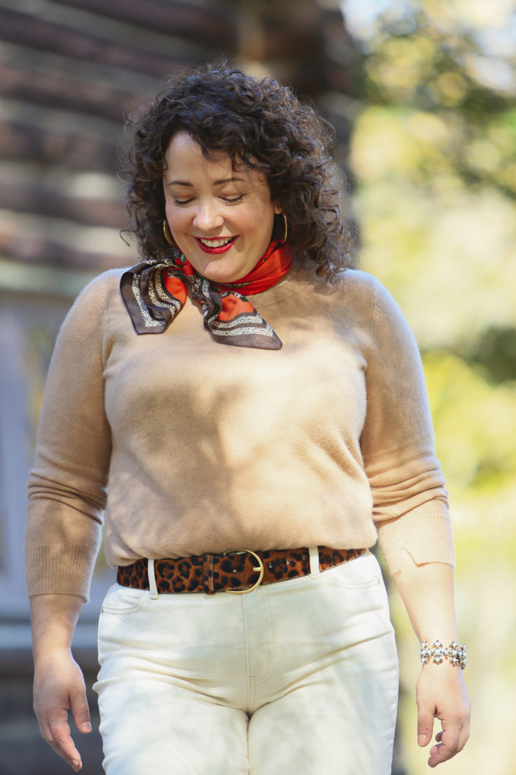 woman looking down, wearing an orange printed silk scarf at her throat