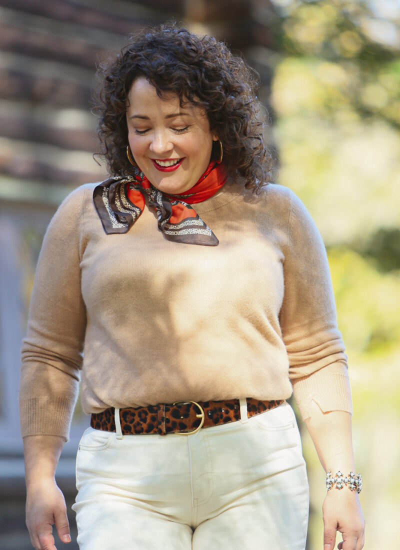 woman looking down, wearing an orange printed silk scarf at her throat