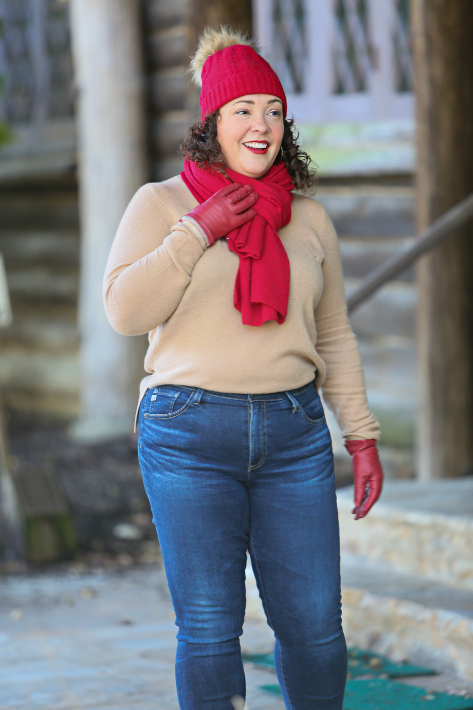 Woman in cream sweater, red scarf and hat and gloves smiling and looking away