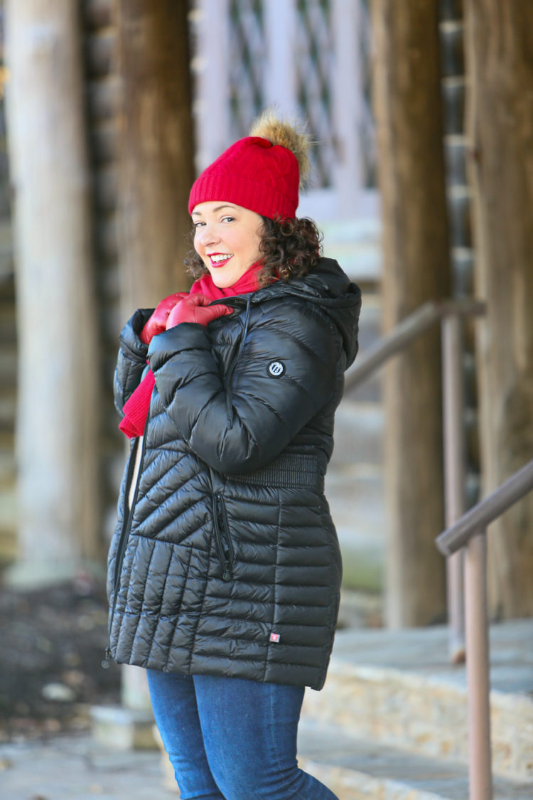 Woman in black puffer coat with red scarf and red hat looking at the camera