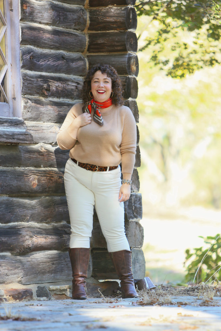 woman in a camel colored sweater, cream jeans, and brown knee-high boots walking towards the camera