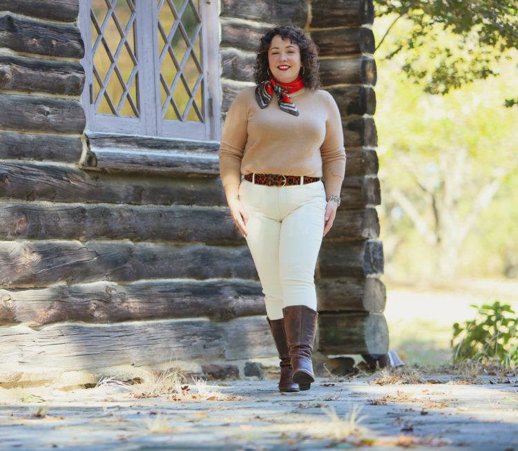 woman in a camel colored sweater, cream jeans, and brown knee-high boots walking towards the camera