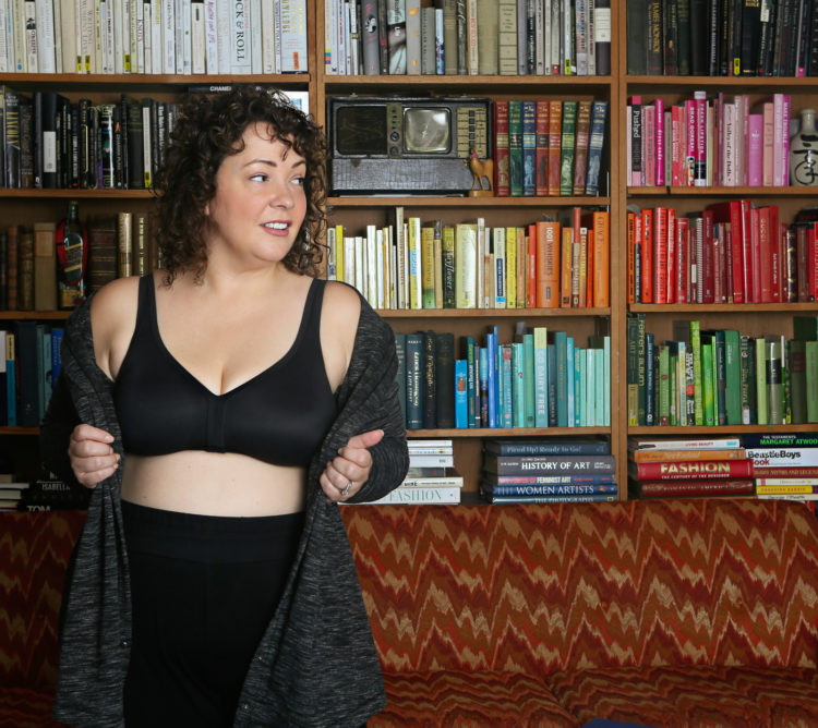 woman in a black wireless bra and black knit pants standing in front of a colorful bookcase