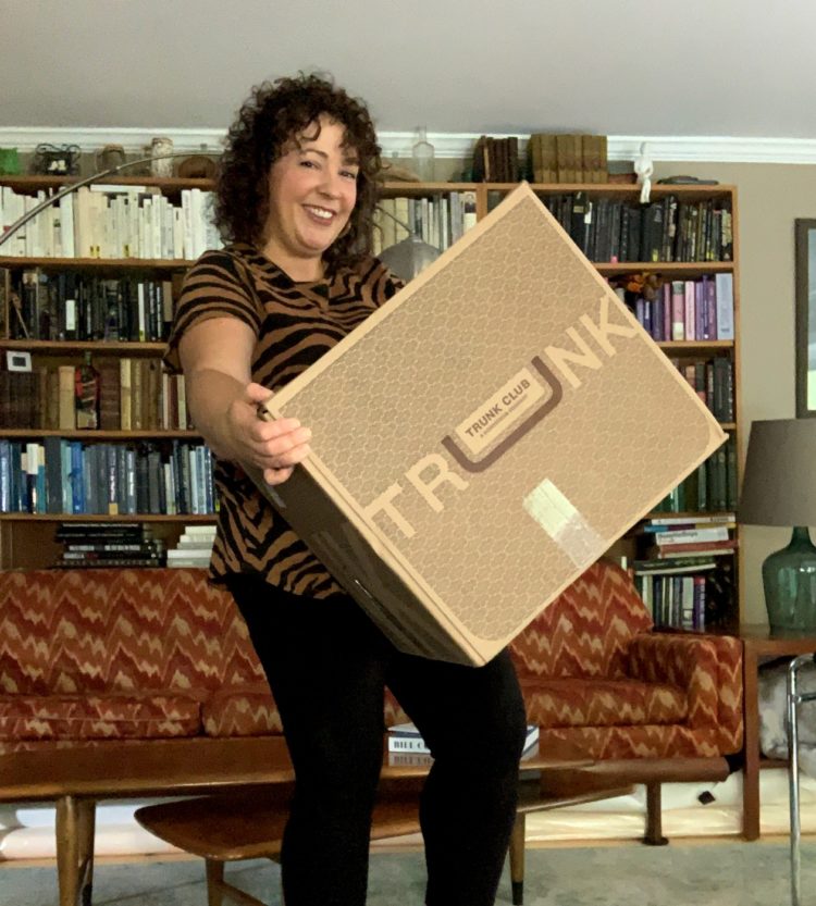 image of woman smiling while holding a large cardboard box that says Trunk Club on it