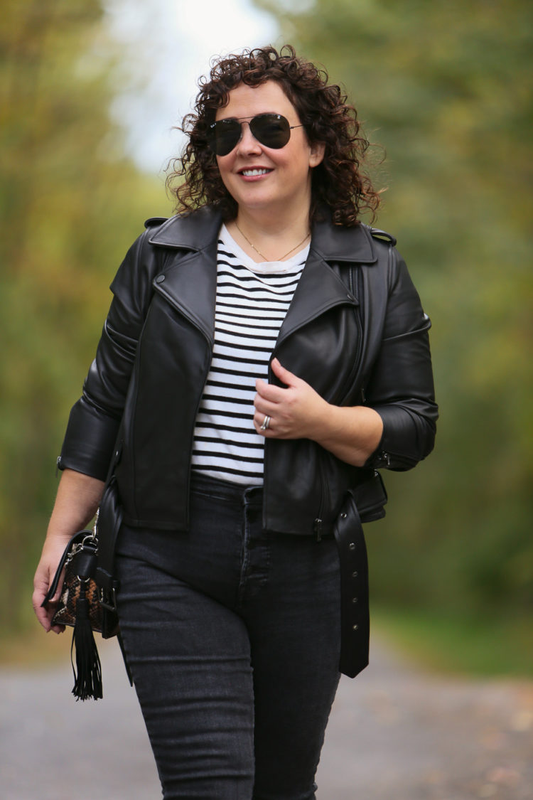 Alison in a black leather moto jacket, black and cream striped tee, gray jeans and white sneakers walking a small brown and white dog