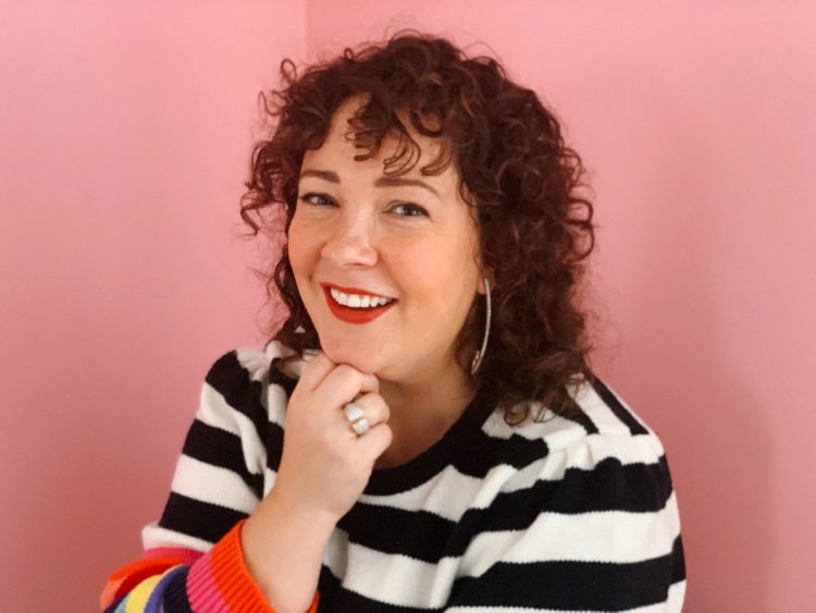 woman with curly hair standing in front of a pink wall