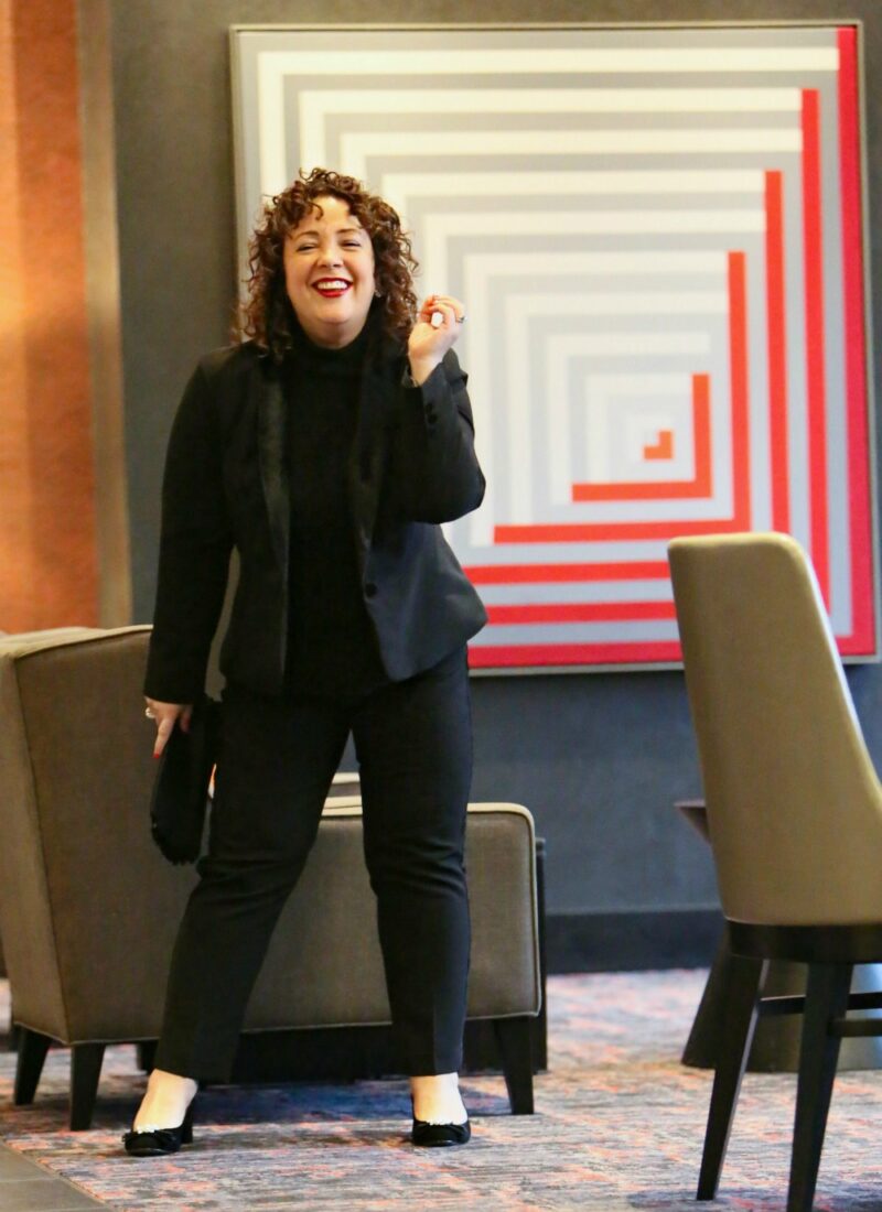 Woman in a black pantsuit with black cashmere and a black suede clutch in her hand