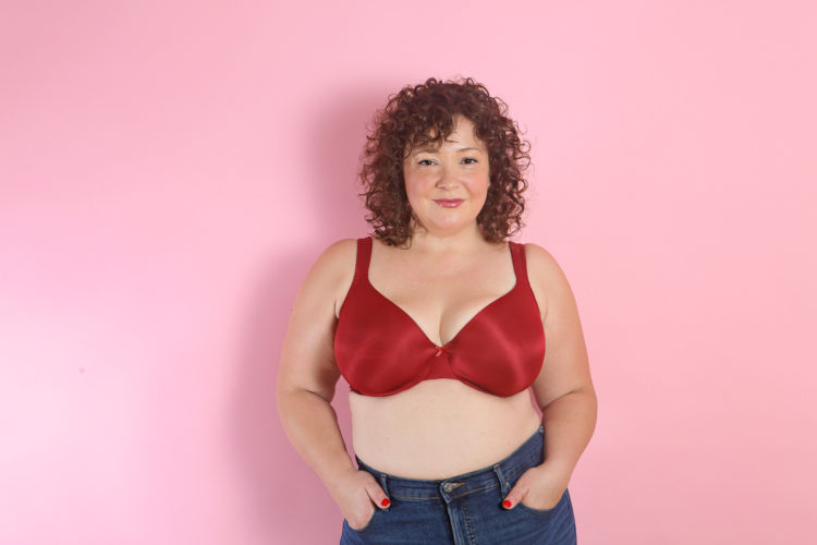 woman in a red bra with her hands in the front pockets of her jeans looking straight into the camera