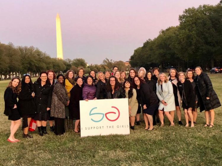 several women standing in front of the washington monument holding a sign that says I Support The Girls