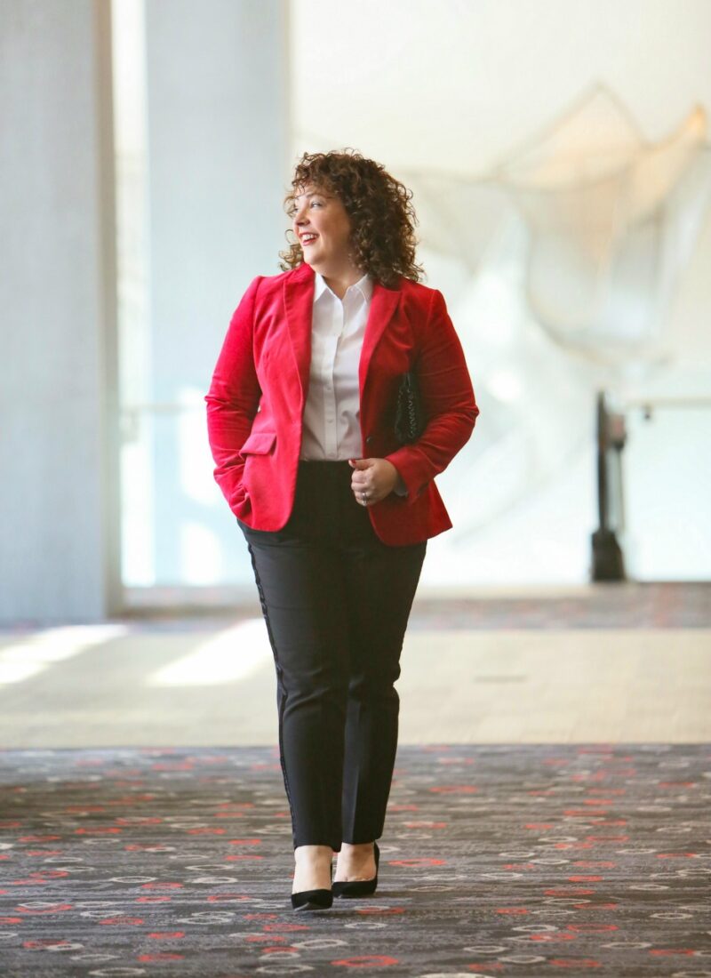 Alison in a red velvet blazer looking out the window of a hotel lobby