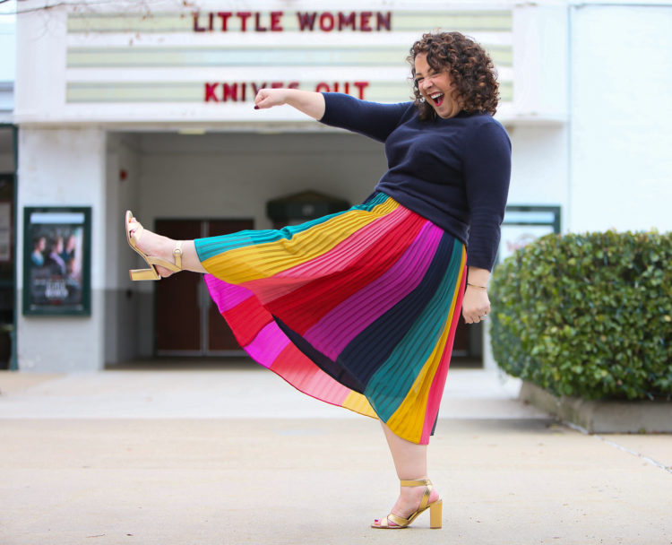 woman in a rainbow striped skirt and navy sweater standing in front of a movie theater