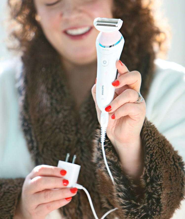 Woman holding up the Philips SatinShave razor and showing it with the charging cord