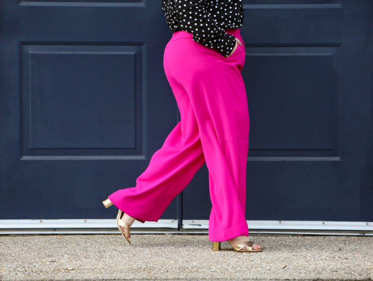 Woman in hot pink wide leg pants and gold Margaux heels walking past a blue door