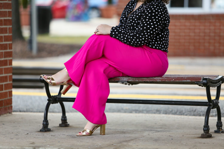 woman in pink pants and a black and white blouse with her legs crossed