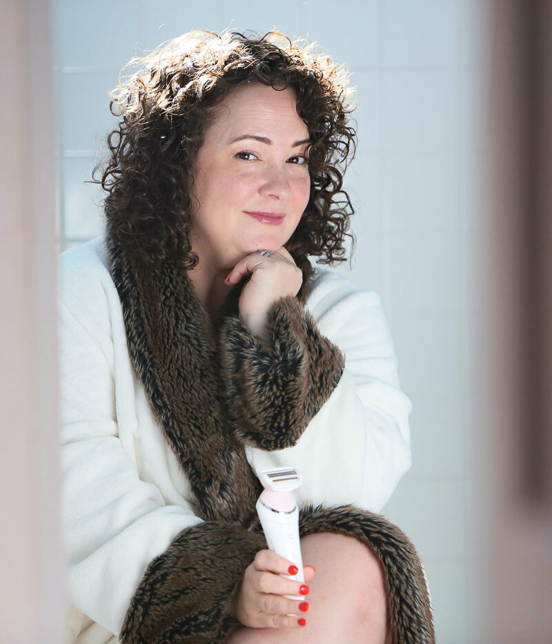 woman in bathrobe smiling at the camera while holding an electric razor