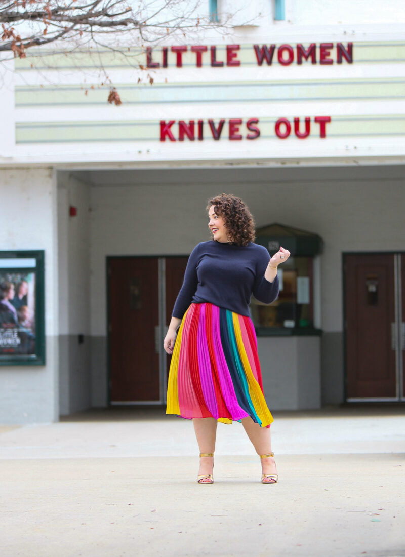 woman in a rainbow striped skirt and navy sweater standing in front of a movie theater