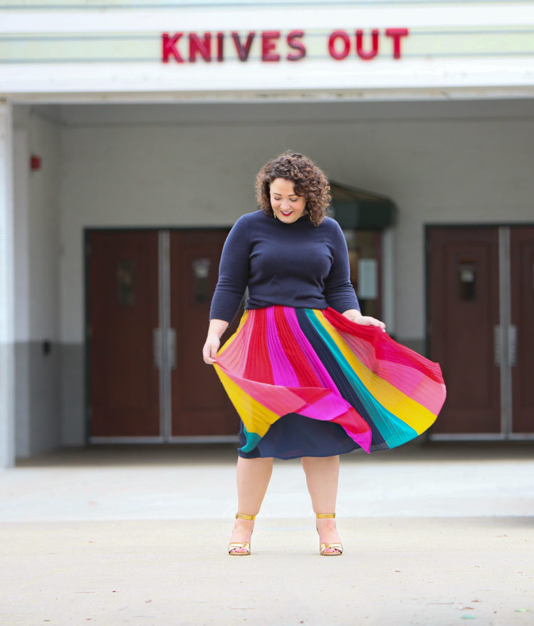 woman in a rainbow striped skirt and navy sweater standing in front of a movie theater