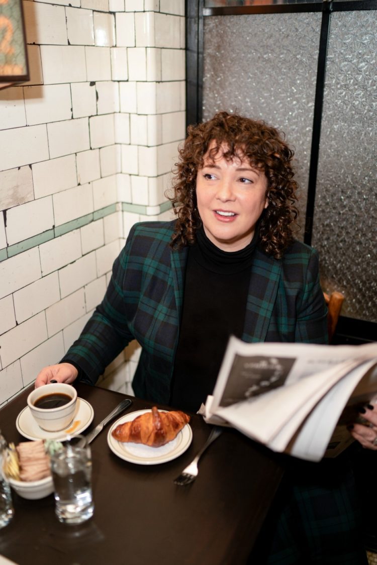 Alison Gary of Wardrobe Oxygen in a Talbots plaid blazer and black turtleneck enjoying a croissant and cup of coffee at Pastis NYC