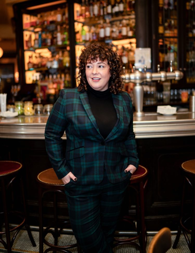 woman in a green plaid pantsuit standing in front of a bar at a French restaurant