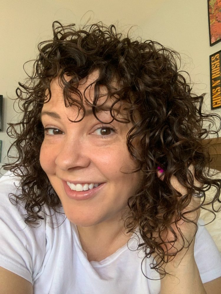 woman smiling at camera with her hand in her dark curly hair