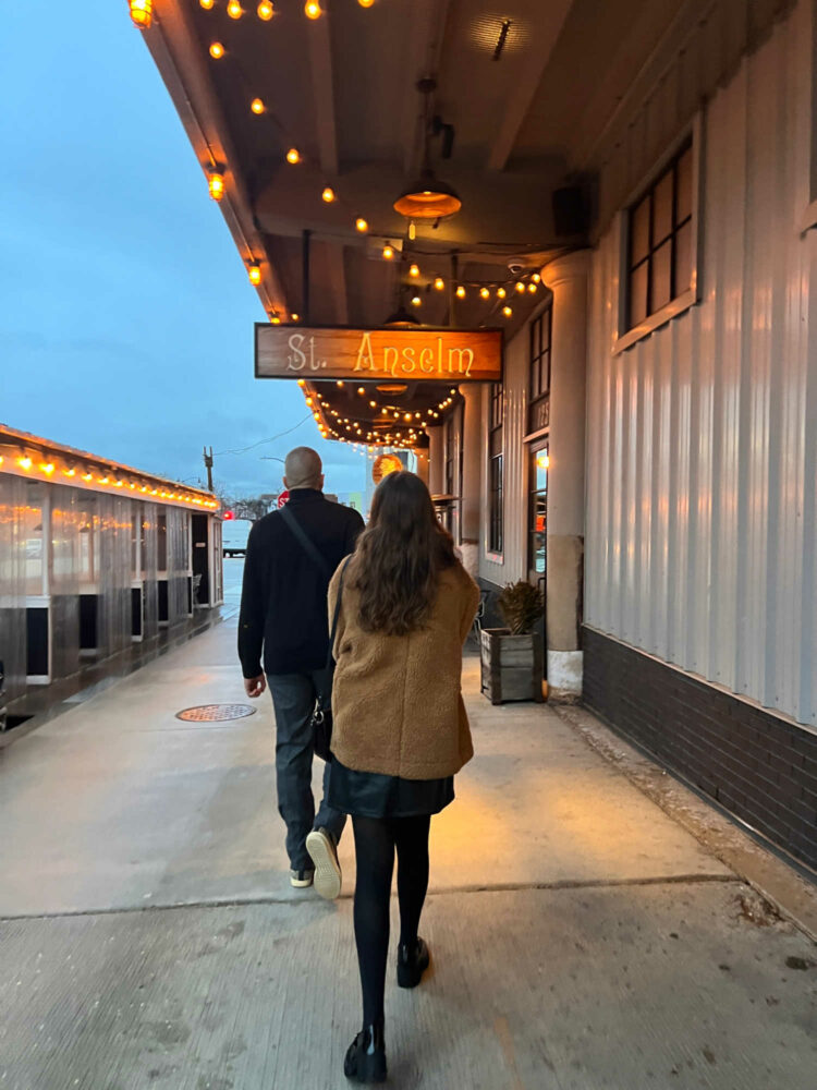 A woman and man in winter coats walking to the door of the restaurant St. Anselm in DC