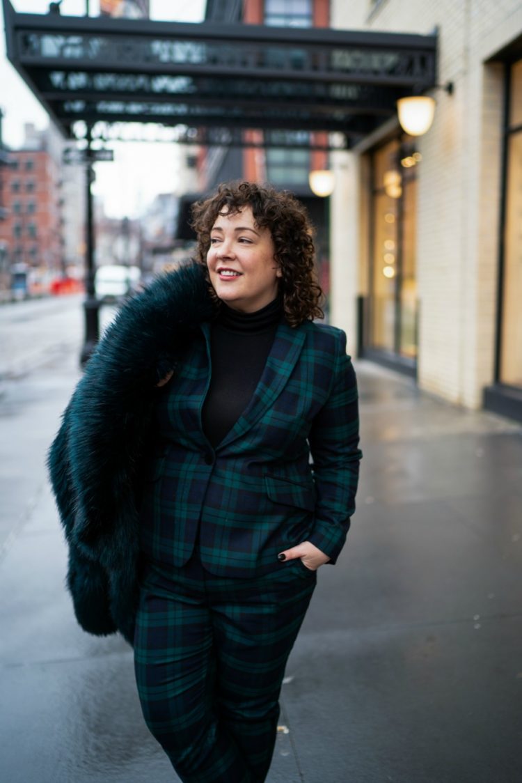 Styling a black watch plaid pantsuit for women with a black turtleneck and dark green faux fur jacket 