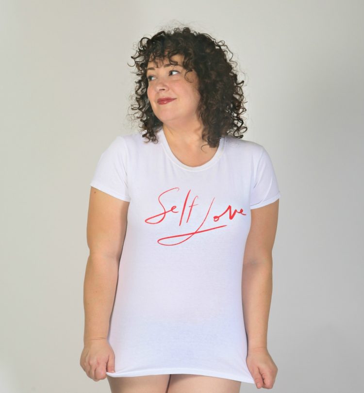 woman wearing a white t-shirt that has the words self love on the front written in red font that looks like handwriting