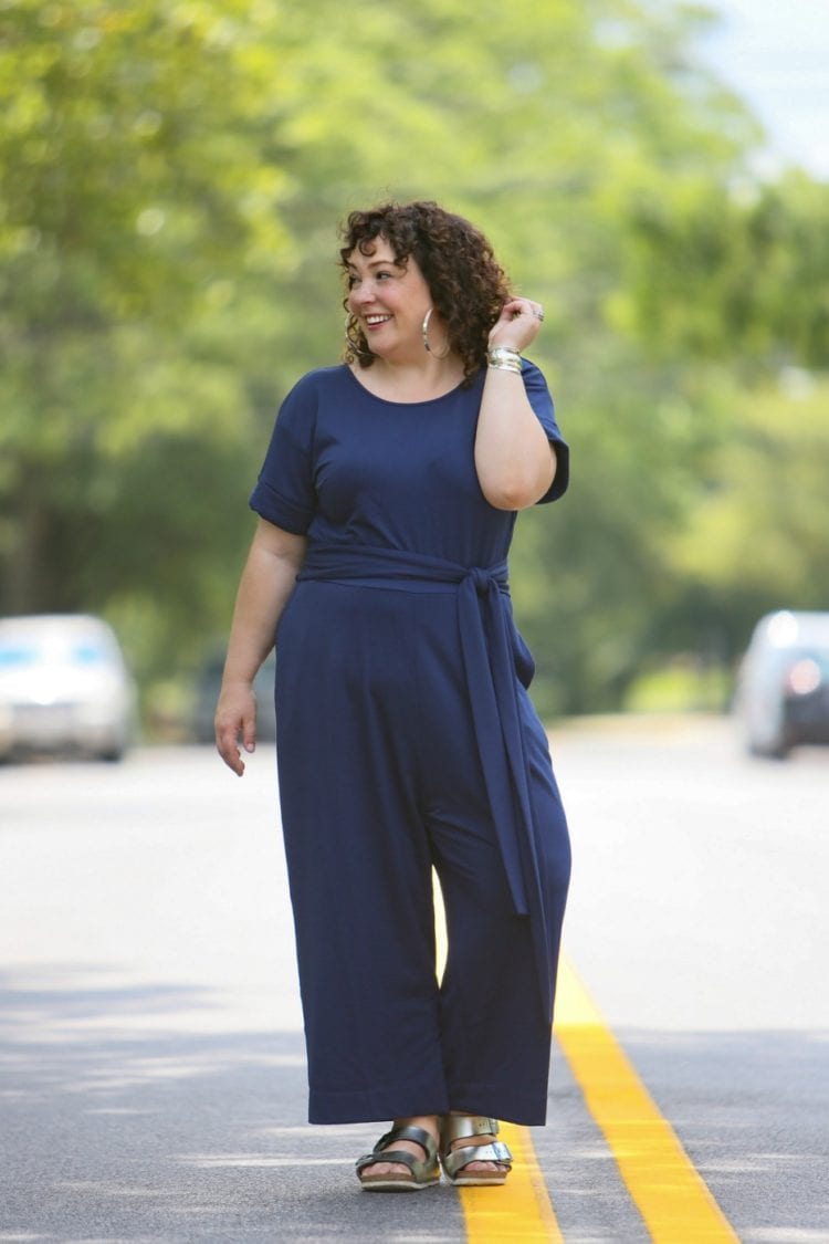 Woman in a dark blue belted jumpsuit from Ori styled with silver metallic Birkenstocks