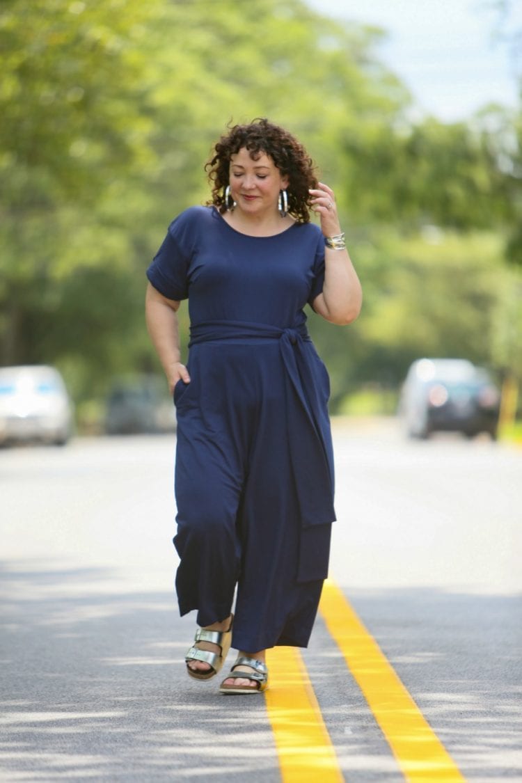 Woman in a dark blue belted jumpsuit from Ori styled with silver metallic Birkenstocks