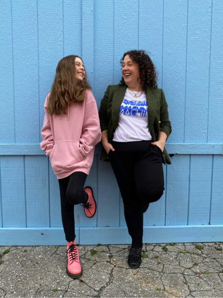 On Birthdays, Racism, and Resilience 1 A woman and her tween daughter with their hands in their pockets, laughing with one another while leaning against a wood wall.