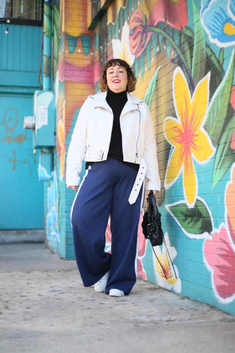 Alison walking towards the camera wearing the white leather jacket over a black turtleneck and navy wide leg ponte pants.