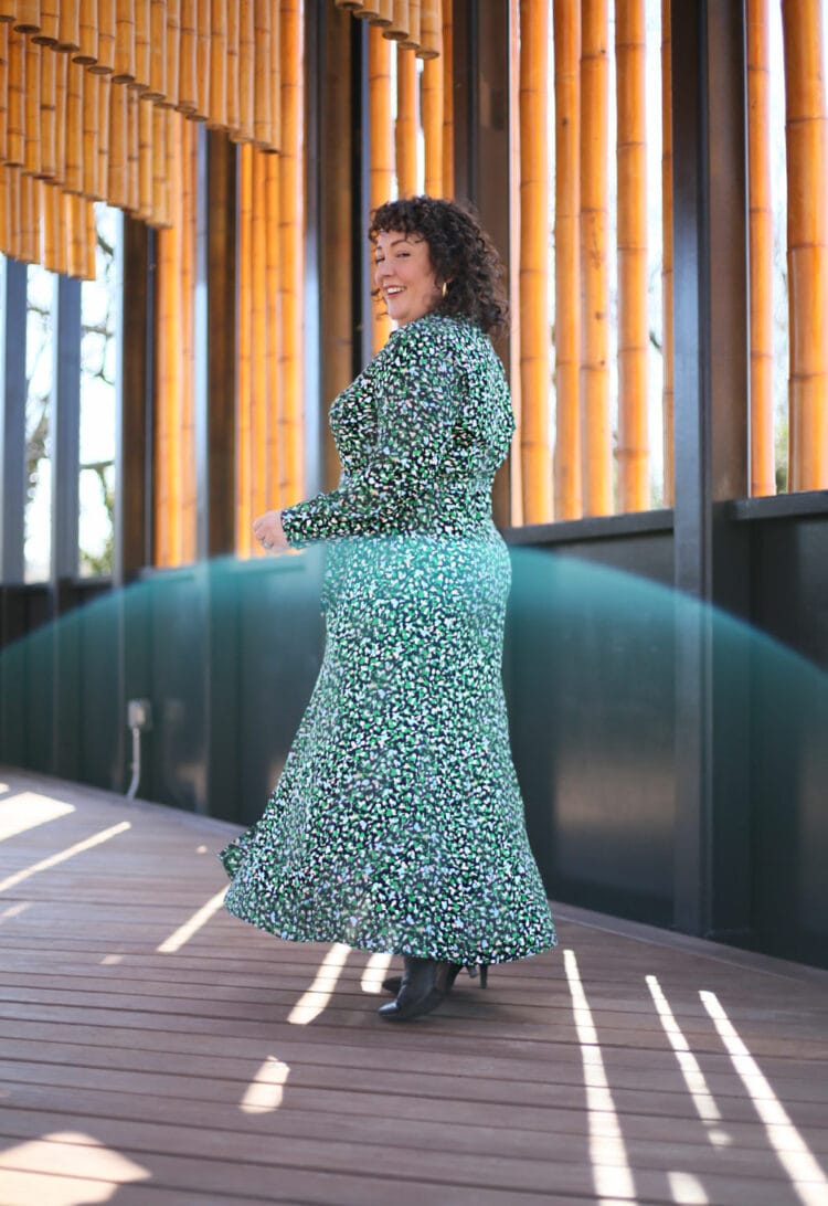 Alison walking away from the camera wearing a green printed calf length belted dress