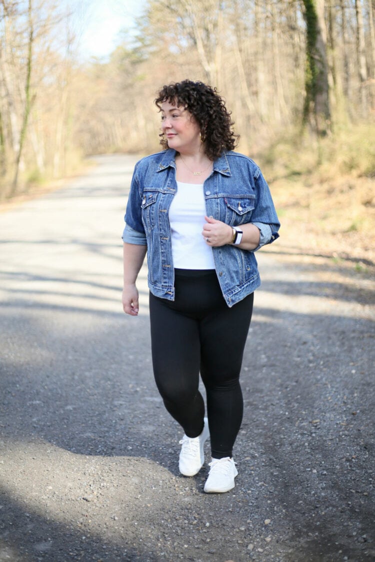 Alison of Wardrobe Oxygen walking down a gravel road in black plus sized leggings from Pari Passu with a vintage Levi's denim jacket and white sneakers