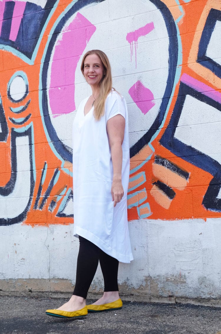 Lissa in the white Tiny Closet Tourist Dress against a colorful brick mural