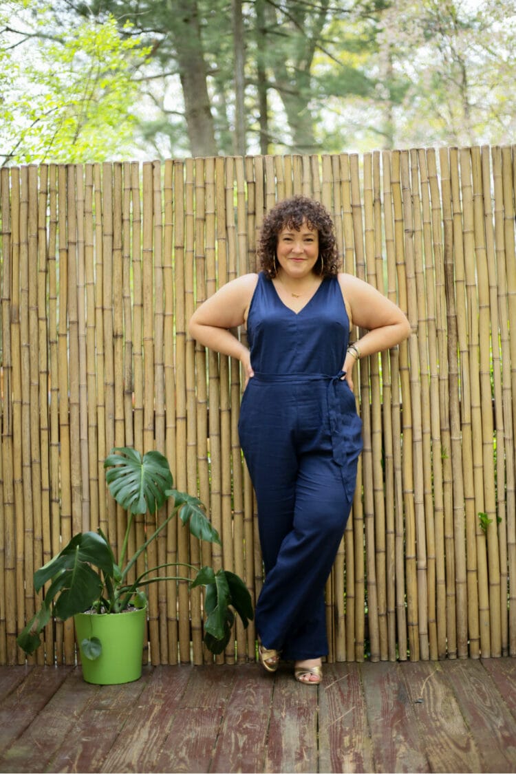 Alison wearing the Universal Standard Luna linen jumpsuit in navy. She is standing outside in front of a bamboo wall