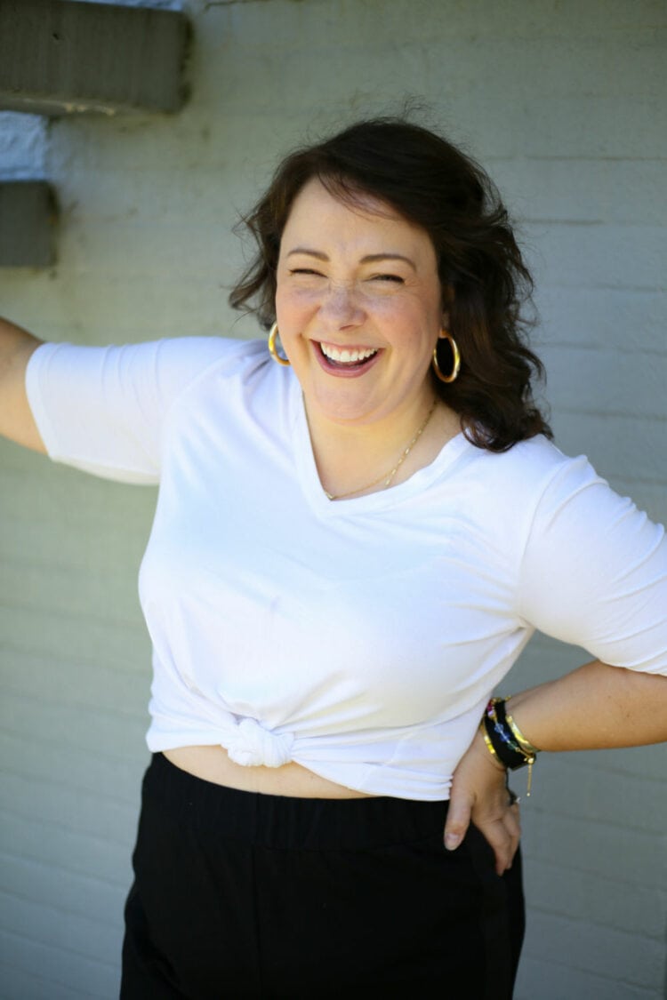 Alison in the Universal Standard Lily Liquid Jersey V-Neck from Universal Standard, tied at the waist. She has one hand on her hip and is laughing to the camera.