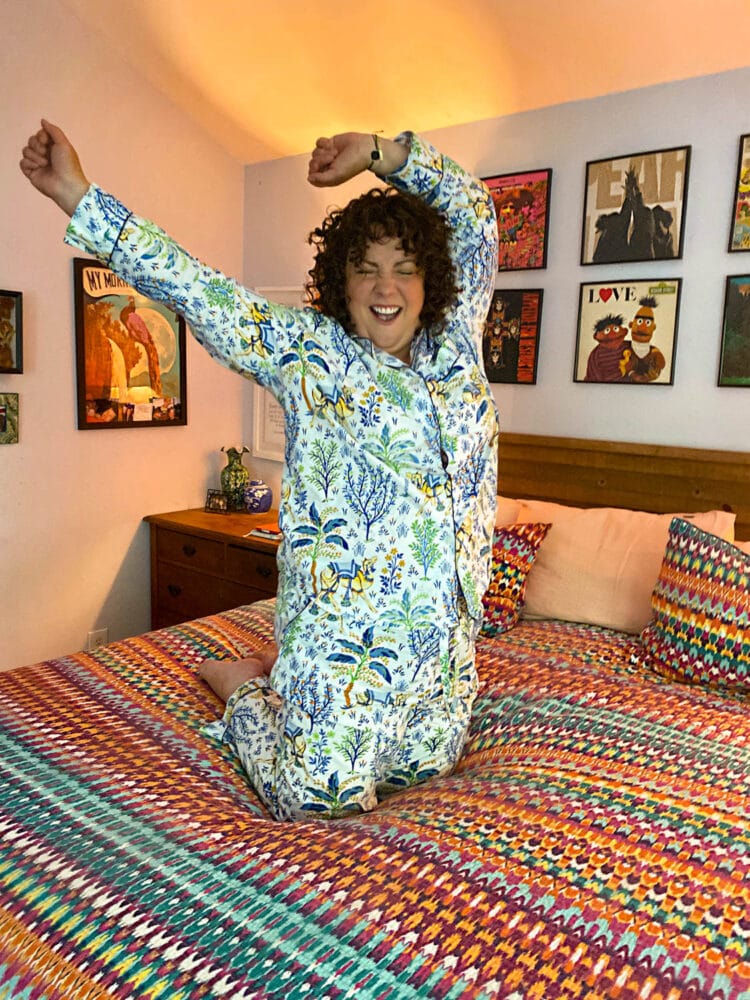 Alison in Printfresh Pajamas, kneeing on her bed and cheering with her hands above her head