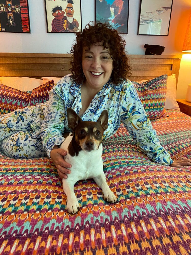 Alison sitting on her bed with her dog Oscar. She is wearing Printfresh pajamas and smiling at the camera