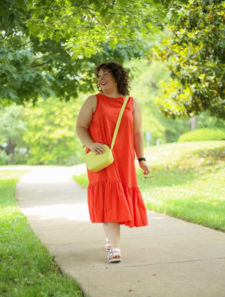 Alison wearing the Christopher John Rogers for Target Orange Shift Dress with a lemon yellow crossbody bag. She is walking down a sidewalk and smiling off camera