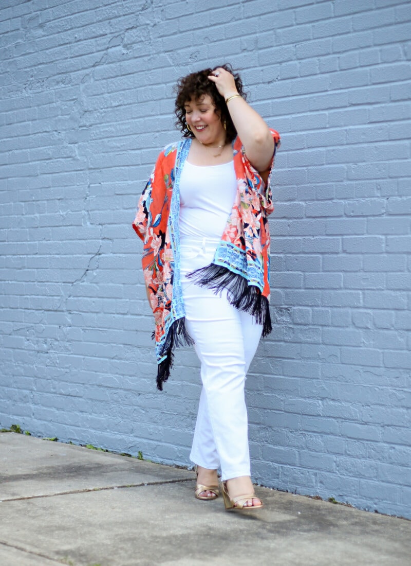 Alison in an orange and blue linen ruana with white jeans and a white tank and gold Margaux Uptown sandals