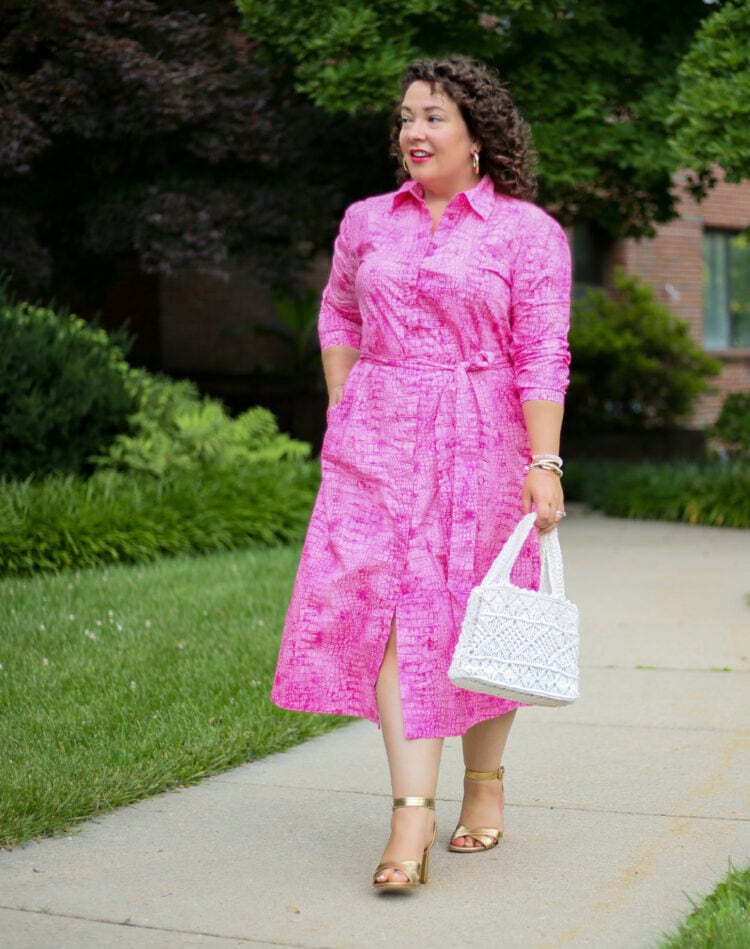 Alison in a pink snakeskin cotton poplin shirtdress from Chico's Black Label collection. She is walking down a sidewalk looking away from the camera.