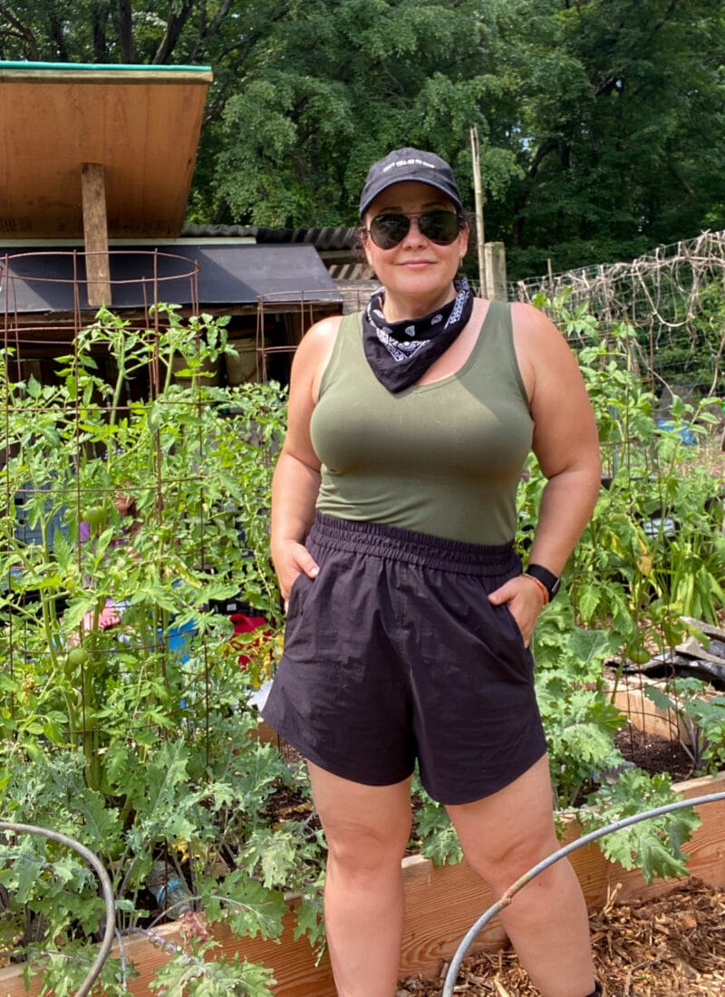 IMO the best size-inclusive active shorts are the Universal Standard Sunny Swim Shorts which I am wearing here in black with an olive fitted tank while working in my garden.