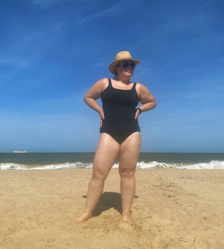 Alison standing on the beach in a black Lands End Tugless tank with her hands on her hips looking off into the distance.