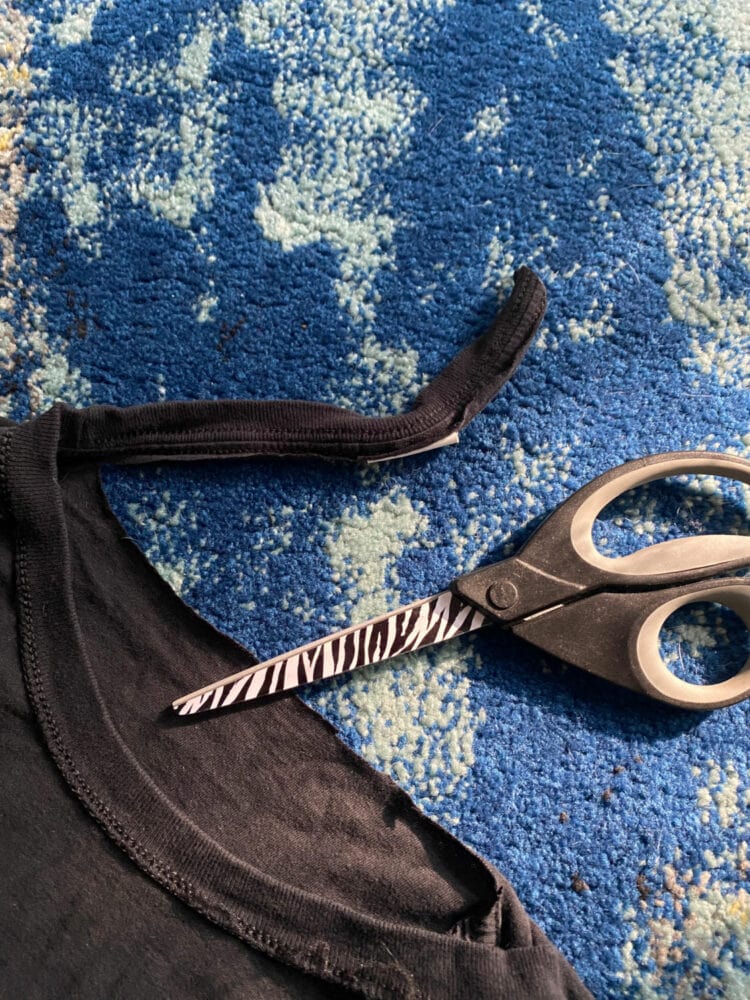 a pair of scissors with a black t-shirt that has half the neckband cut off