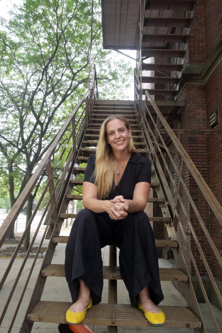 woman with long blonde hair wearing a black linen jumpsuit and yellow leather flats, sitting on an outdoor set of stairs