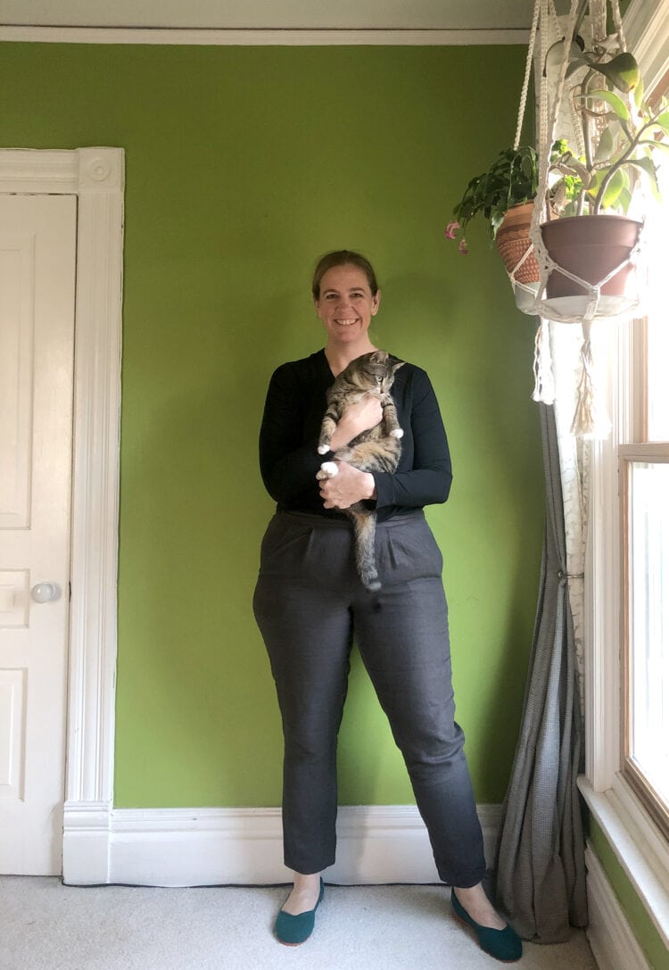 Woman in black t-shirt and charcoal colored ankle pants, holding a cat