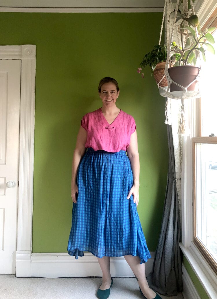 Woman in a pink linen short sleeve top tucked in a blue check midi length skirt