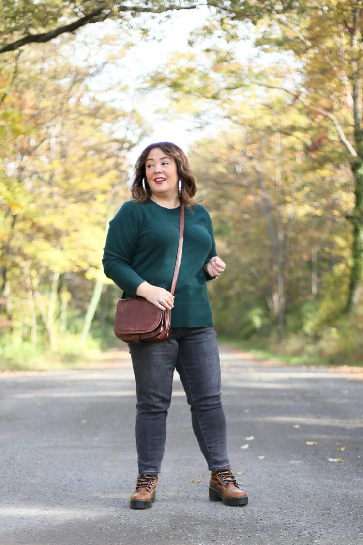 Alison is wearing the same green cashmere sweater in other photos but now it is untucked and styled with dark gray skinny jeans and brown Dr. marten boots.