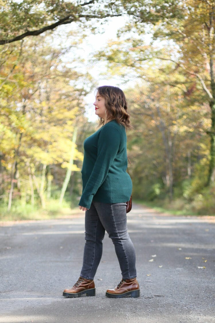Alison in a green untucked cashmere sweater and dark gray jeans, walking to the left